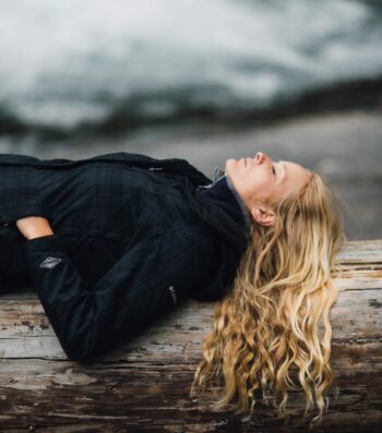 woman in black zip-up jacket leaning on large log at daytime